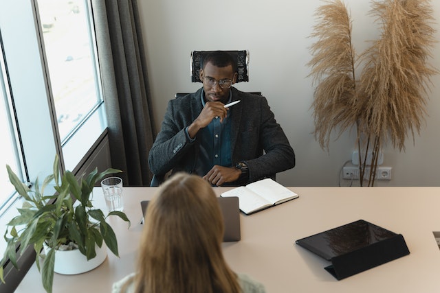 A man sat at a desk during a job interview, facing a woman
